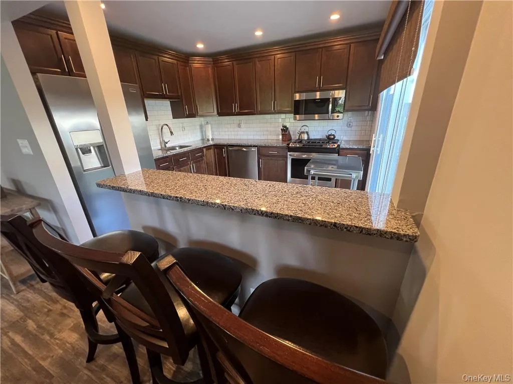 Kitchen with light stone counters, stainless steel appliances, dark wood-type flooring, and kitchen peninsula Kitchen with light stone counters, stainless steel appliances, dark wood-type flooring, and kitchen peninsula