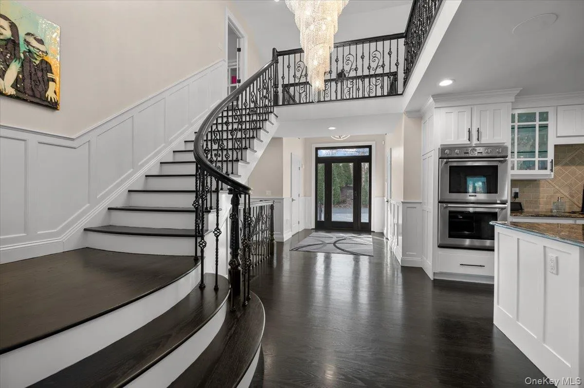 Foyer entrance featuring a decorative wall, wainscoting, dark wood-style flooring, a chandelier, and stairway Foyer entrance featuring a decorative wall, wainscoting, dark wood-style flooring, a chandelier, and stairway