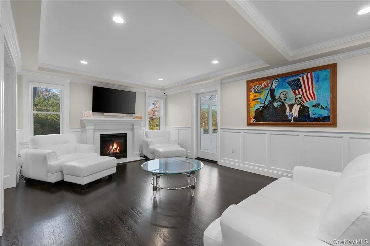 Living room with ornamental molding, a glass covered fireplace, dark wood-style floors, a decorative wall, and a raised ceiling Living room with ornamental molding, a glass covered fireplace, dark wood-style floors, a decorative wall, and a raised ceiling