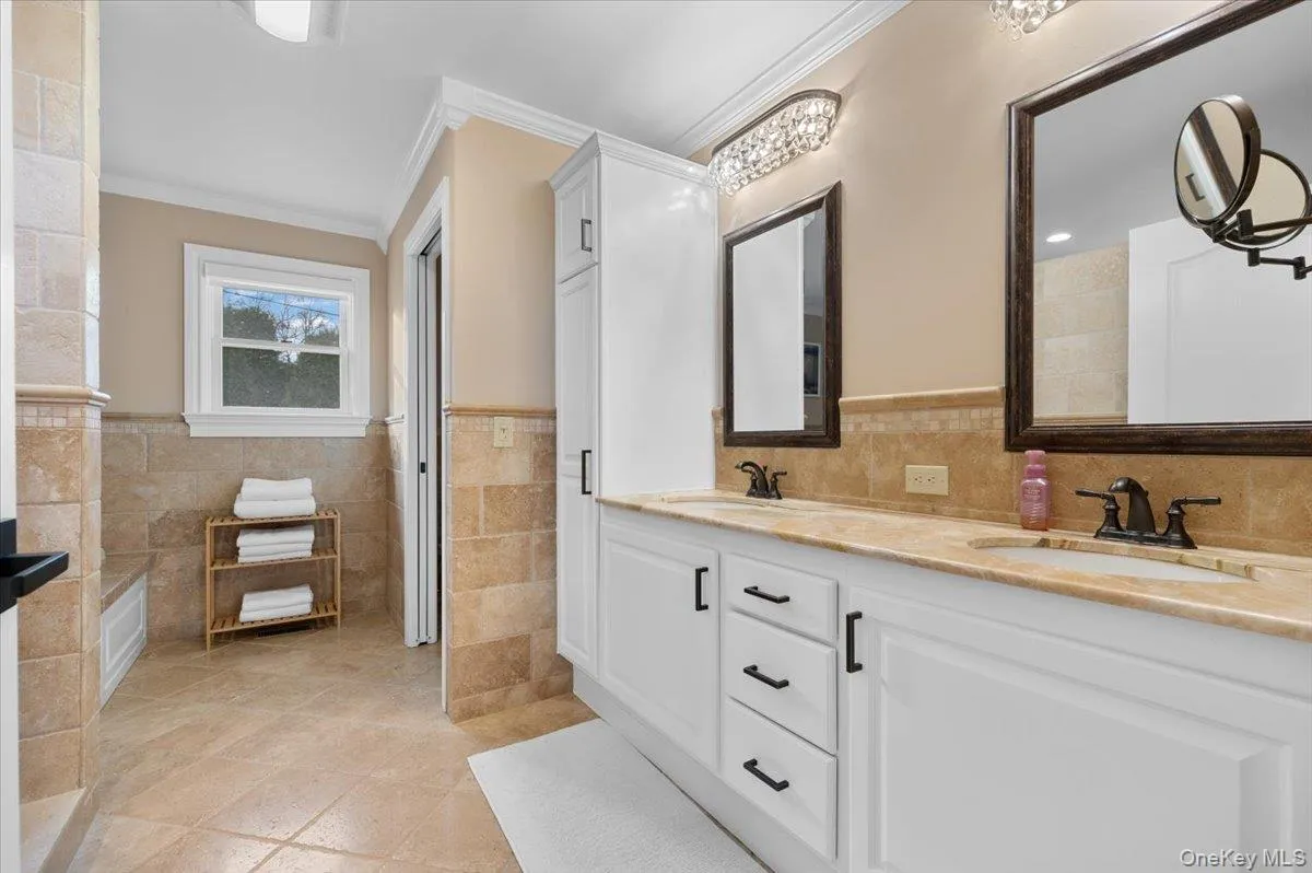Bathroom with double vanity, wainscoting, tile walls, light tile patterned floors, and crown molding Bathroom with double vanity, wainscoting, tile walls, light tile patterned floors, and crown molding