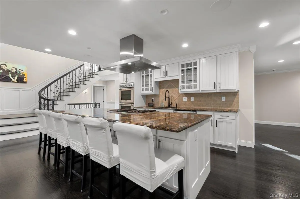 Kitchen with glass insert cabinets, a breakfast bar, island range hood, dark stone countertops, and a large island Kitchen with glass insert cabinets, a breakfast bar, island range hood, dark stone countertops, and a large island