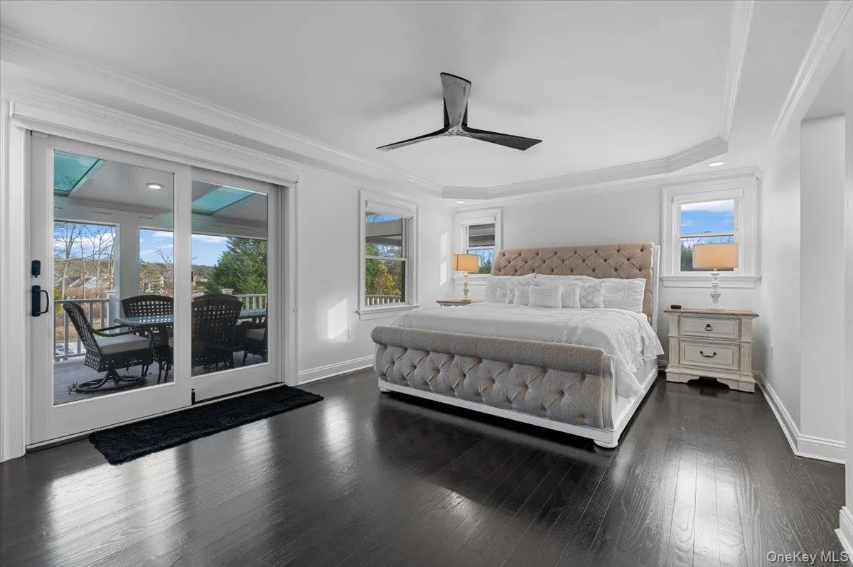 Bedroom featuring crown molding, access to outside, dark wood-style floors, ceiling fan, and a raised ceiling Bedroom featuring crown molding, access to outside, dark wood-style floors, ceiling fan, and a raised ceiling