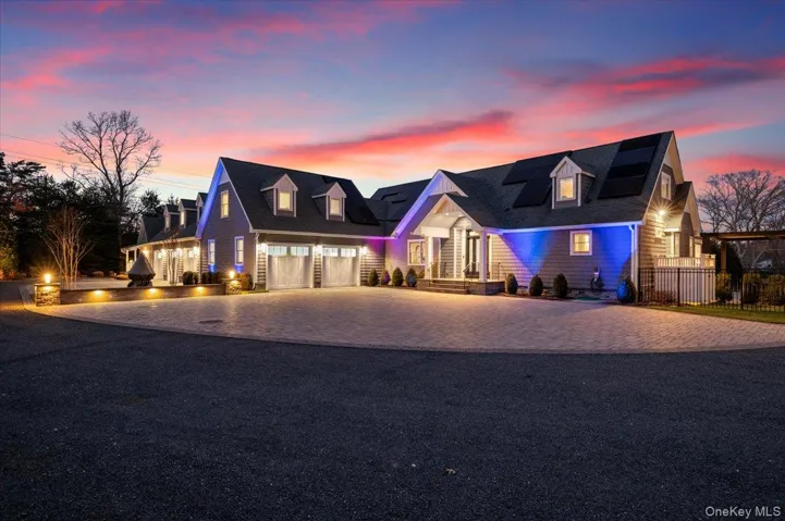 Cape cod house with decorative driveway, a garage, and roof mounted solar panels