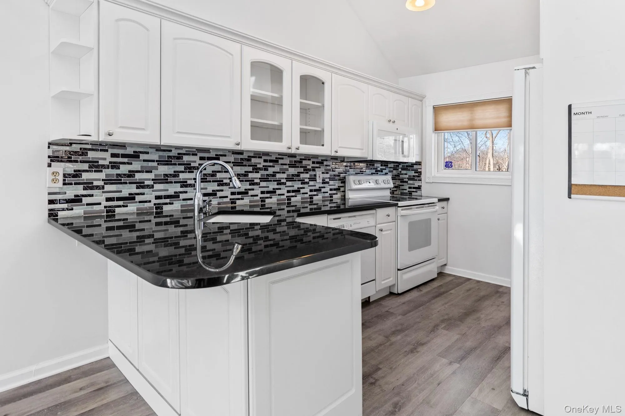 Kitchen featuring glass insert cabinets, white appliances, vaulted ceiling, a peninsula, and white cabinets Kitchen featuring glass insert cabinets, white appliances, vaulted ceiling, a peninsula, and white cabinets