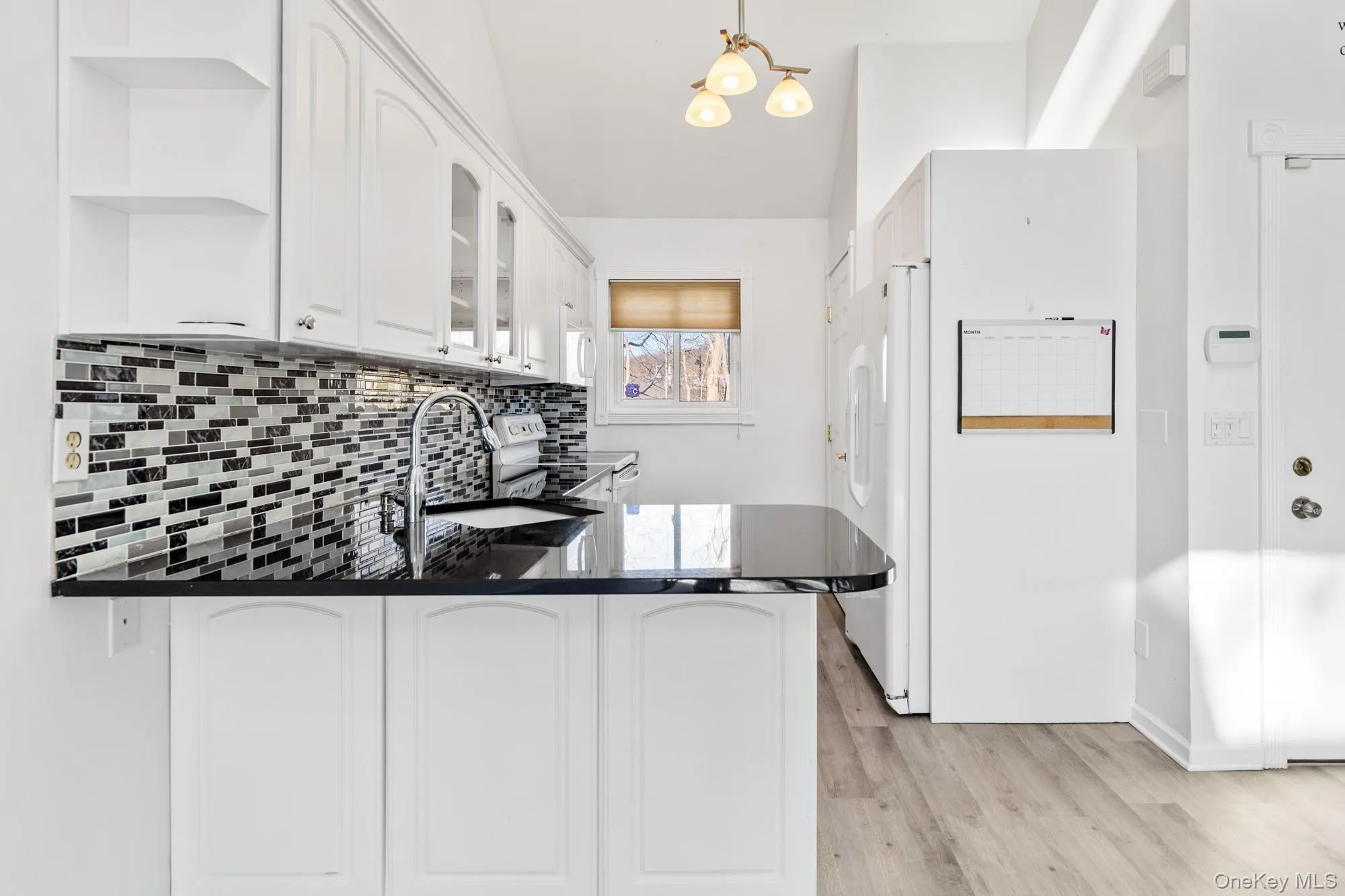 Kitchen featuring white cabinets, white appliances, decorative backsplash, glass insert cabinets, and a peninsula Kitchen featuring white cabinets, white appliances, decorative backsplash, glass insert cabinets, and a peninsula