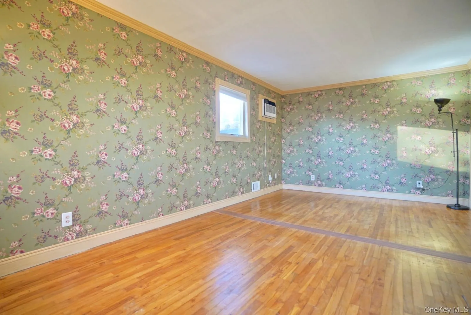 Empty room with wallpapered walls, hardwood / wood-style flooring, and crown molding Empty room with wallpapered walls, hardwood / wood-style flooring, and crown molding