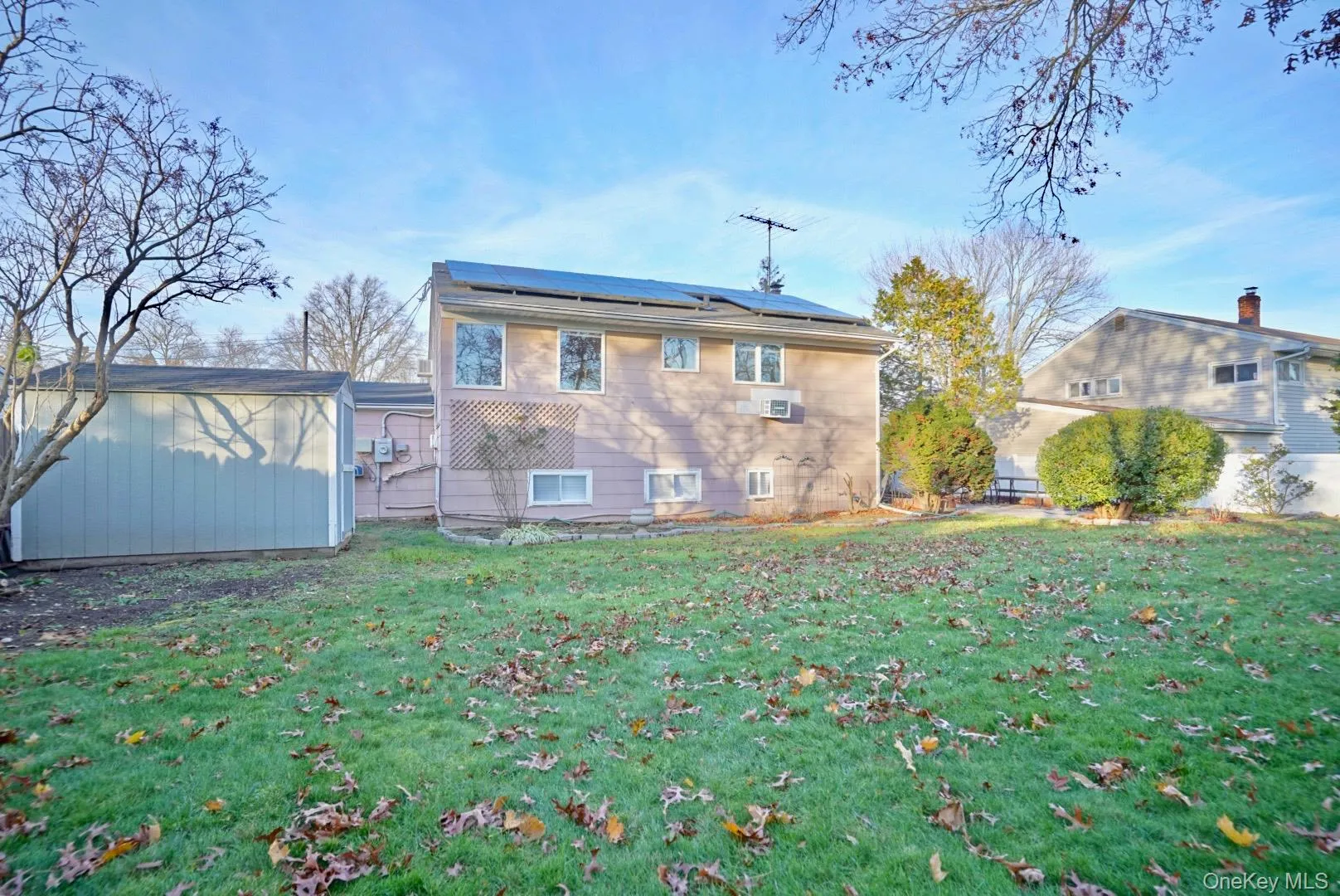 Back of house with a storage unit, solar panels, and a yard Back of house with a storage unit, solar panels, and a yard