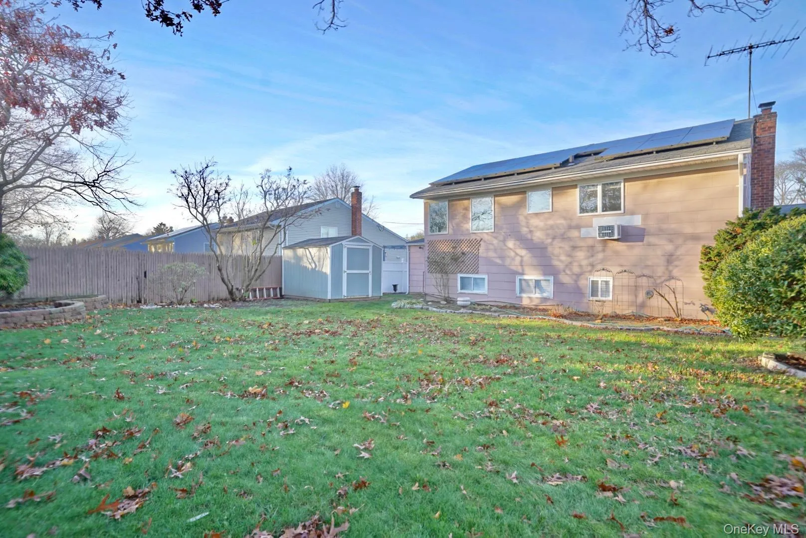 Back of property featuring a storage shed, roof mounted solar panels, a chimney, and a fenced backyard Back of property featuring a storage shed, roof mounted solar panels, a chimney, and a fenced backyard