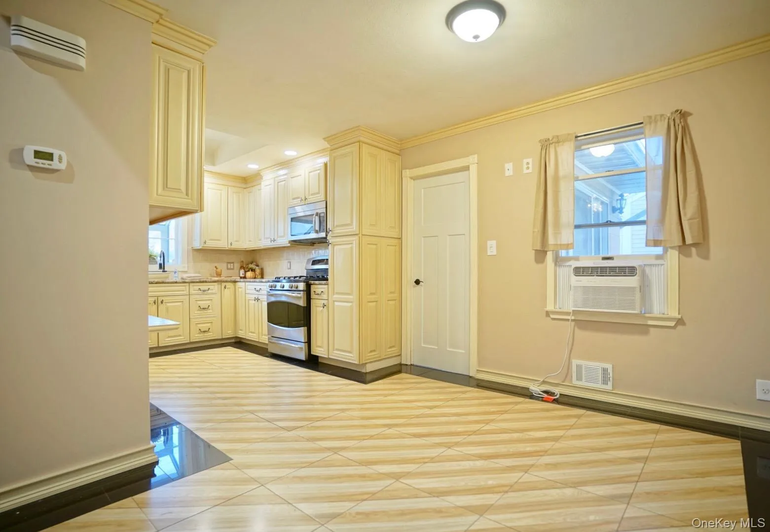 Kitchen with stainless steel appliances, light countertops, cream cabinetry, cooling unit, and recessed lighting Kitchen with stainless steel appliances, light countertops, cream cabinetry, cooling unit, and recessed lighting