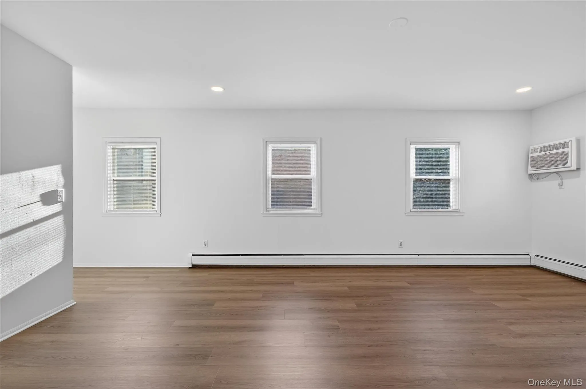 Empty room featuring wood finished floors, recessed lighting, and an AC wall unit Empty room featuring wood finished floors, recessed lighting, and an AC wall unit