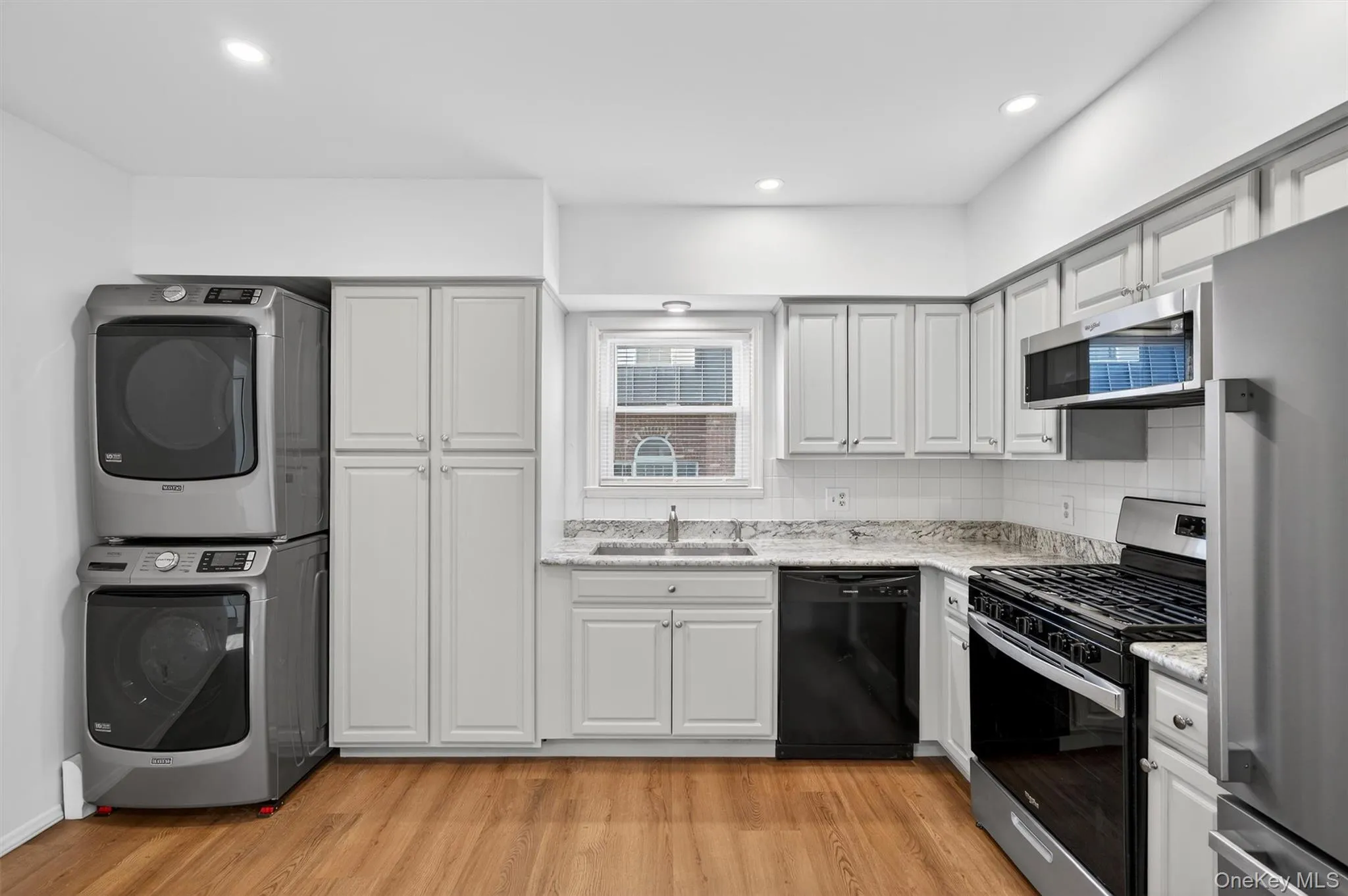 Kitchen with stainless steel appliances, stacked washing machine and dryer, decorative backsplash, light wood-type flooring, and recessed lighting Kitchen with stainless steel appliances, stacked washing machine and dryer, decorative backsplash, light wood-type flooring, and recessed lighting