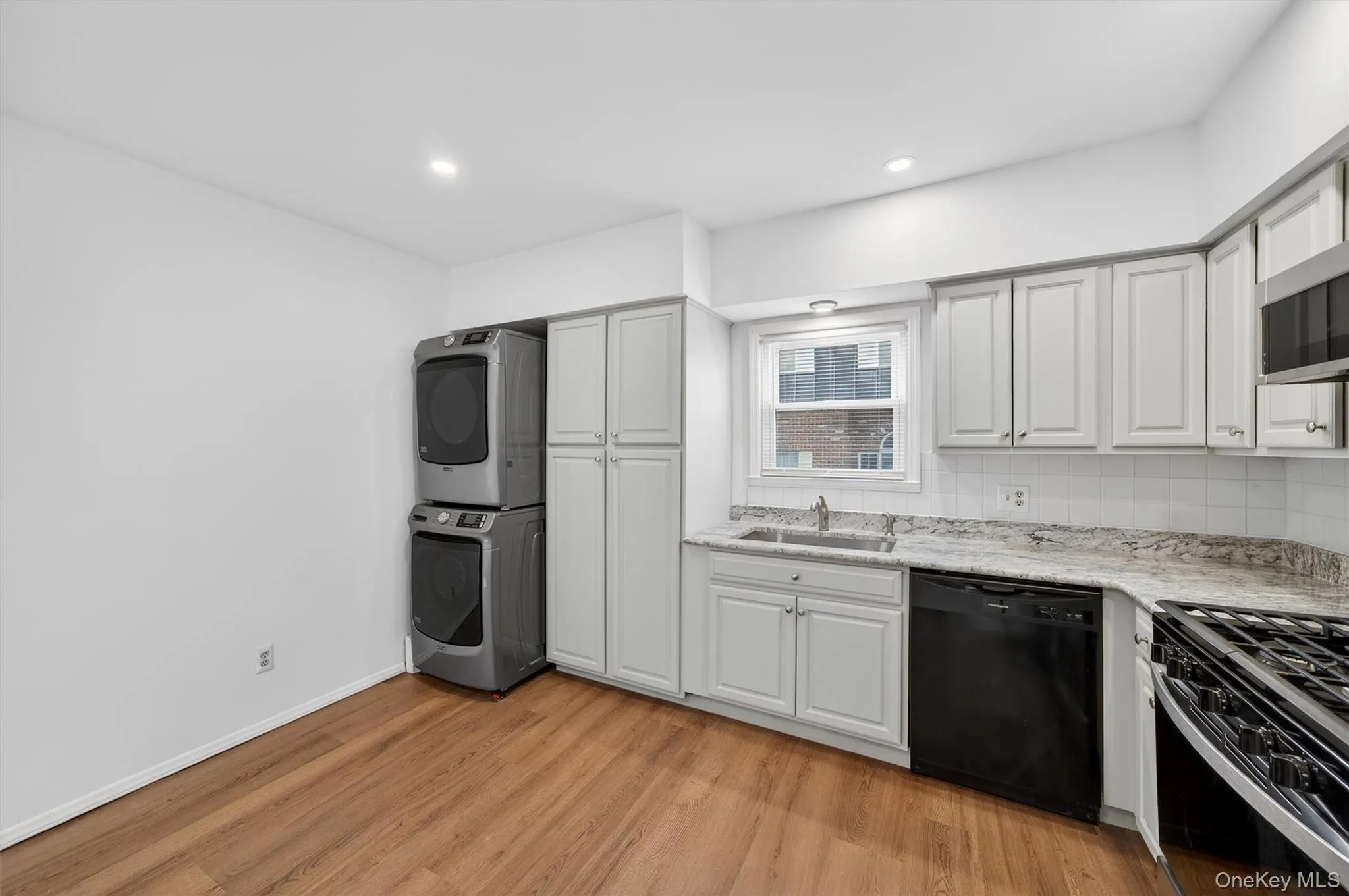 Kitchen featuring black appliances, stacked washer / drying machine, light wood-style flooring, white cabinets, and recessed lighting Kitchen featuring black appliances, stacked washer / drying machine, light wood-style flooring, white cabinets, and recessed lighting