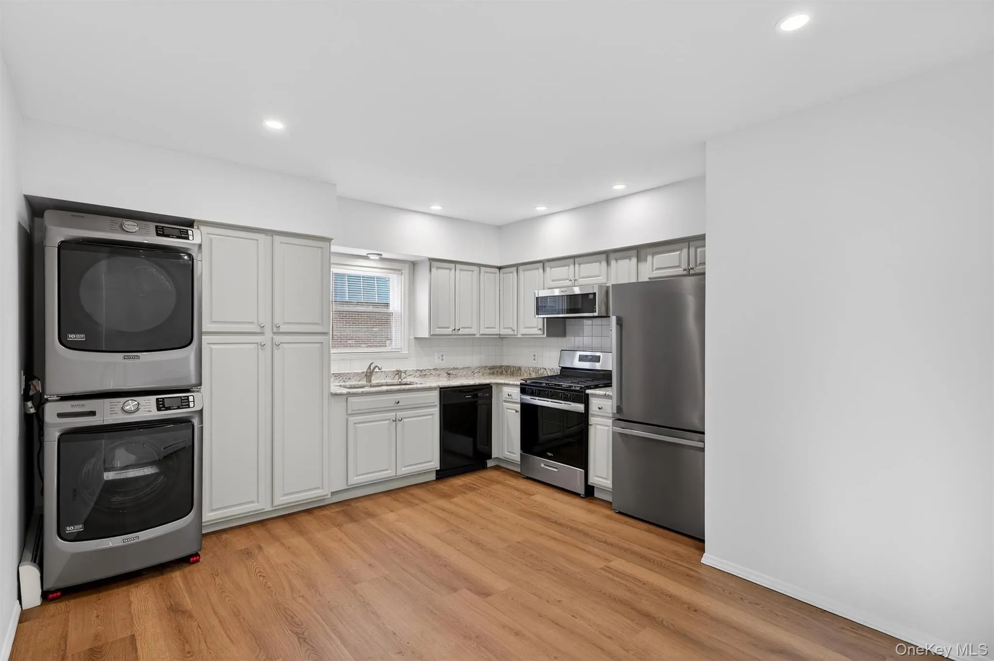 Kitchen featuring appliances with stainless steel finishes, stacked washer and clothes dryer, light wood-style floors, recessed lighting, and tasteful backsplash Kitchen featuring appliances with stainless steel finishes, stacked washer and clothes dryer, light wood-style floors, recessed lighting, and tasteful backsplash