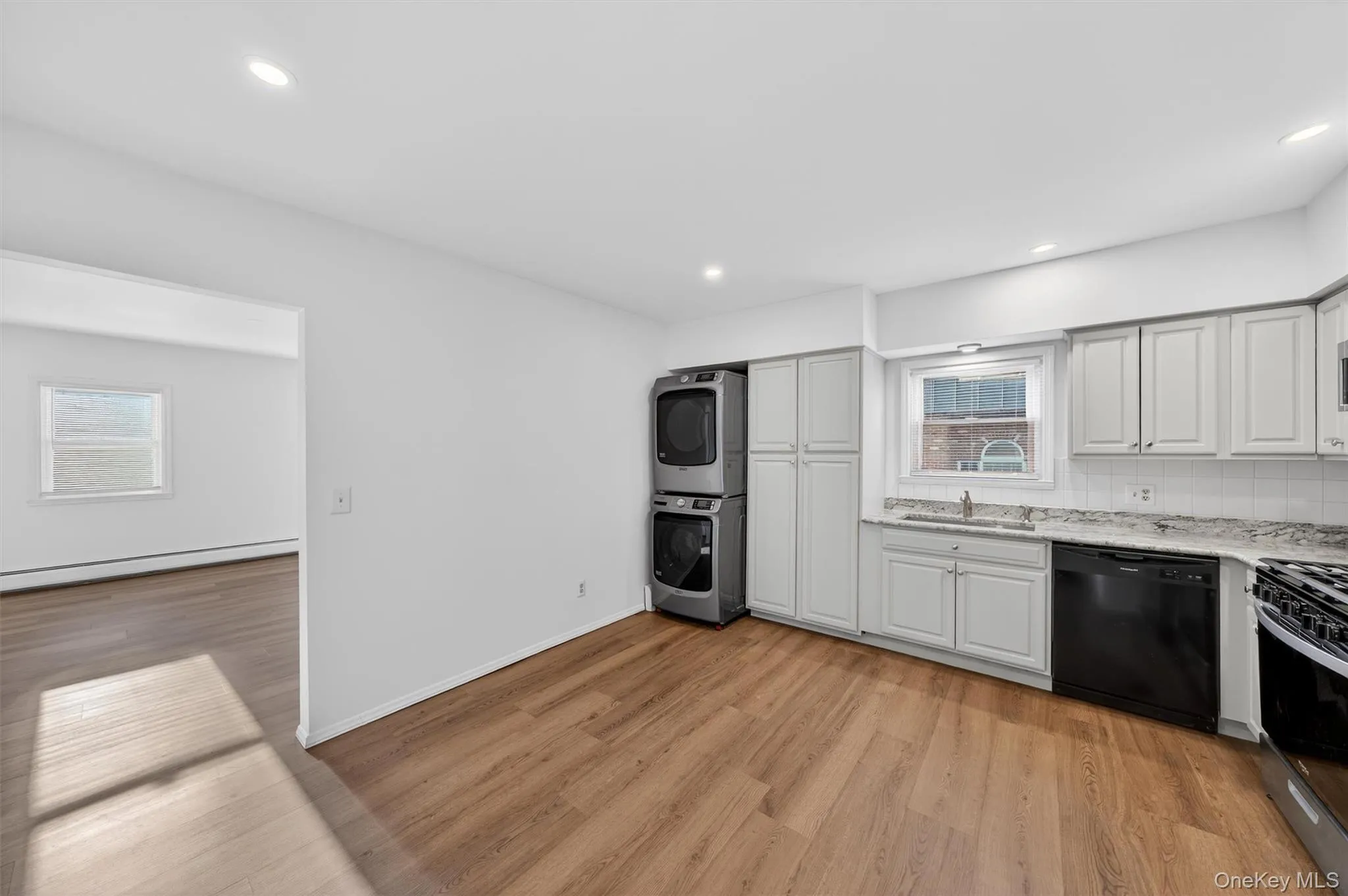 Kitchen with black dishwasher, stainless steel range with gas stovetop, stacked washer / drying machine, white cabinets, and light stone countertops Kitchen with black dishwasher, stainless steel range with gas stovetop, stacked washer / drying machine, white cabinets, and light stone countertops