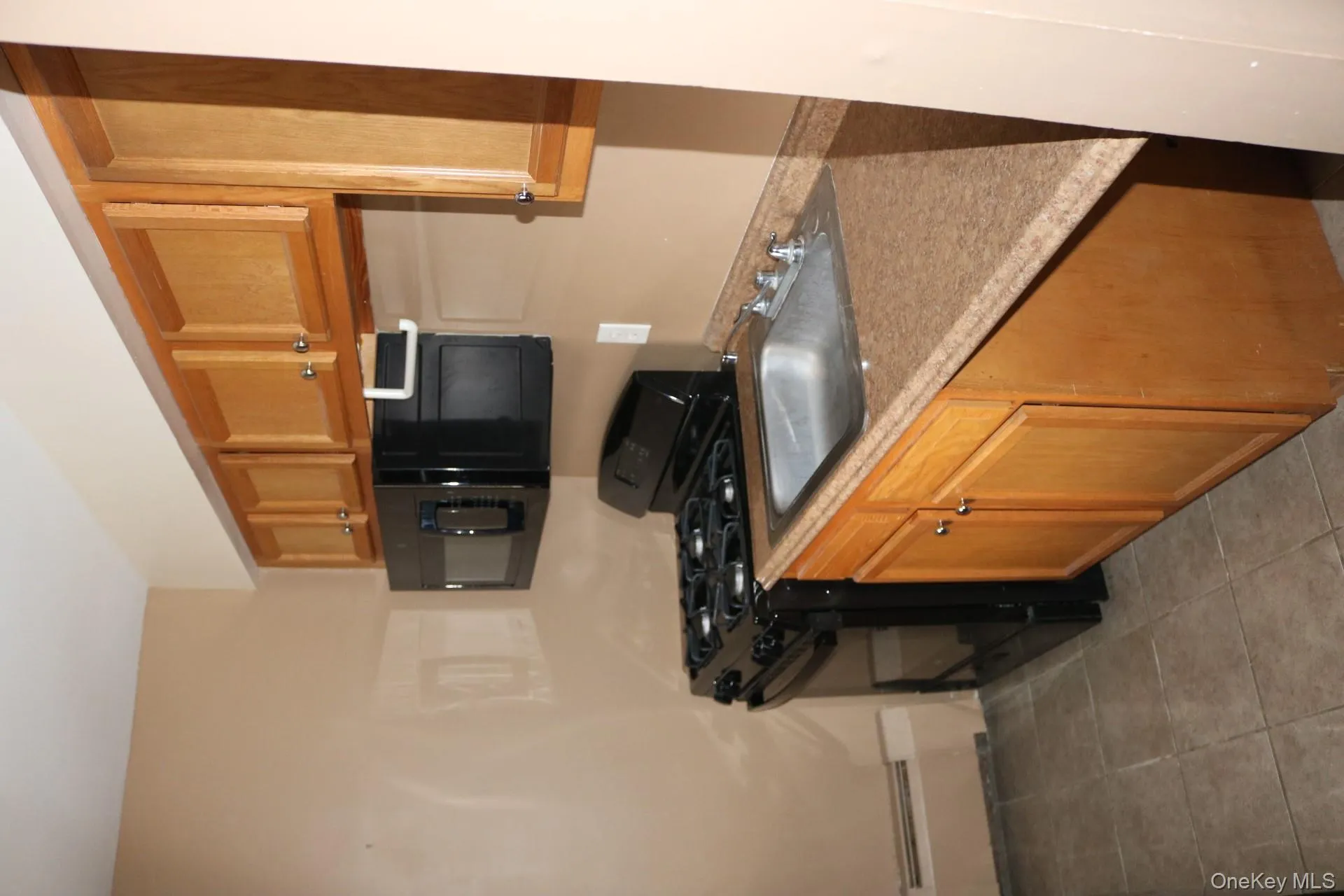 Kitchen with sink, black range oven, light tile patterned floors, and a baseboard heating unit Kitchen with sink, black range oven, light tile patterned floors, and a baseboard heating unit