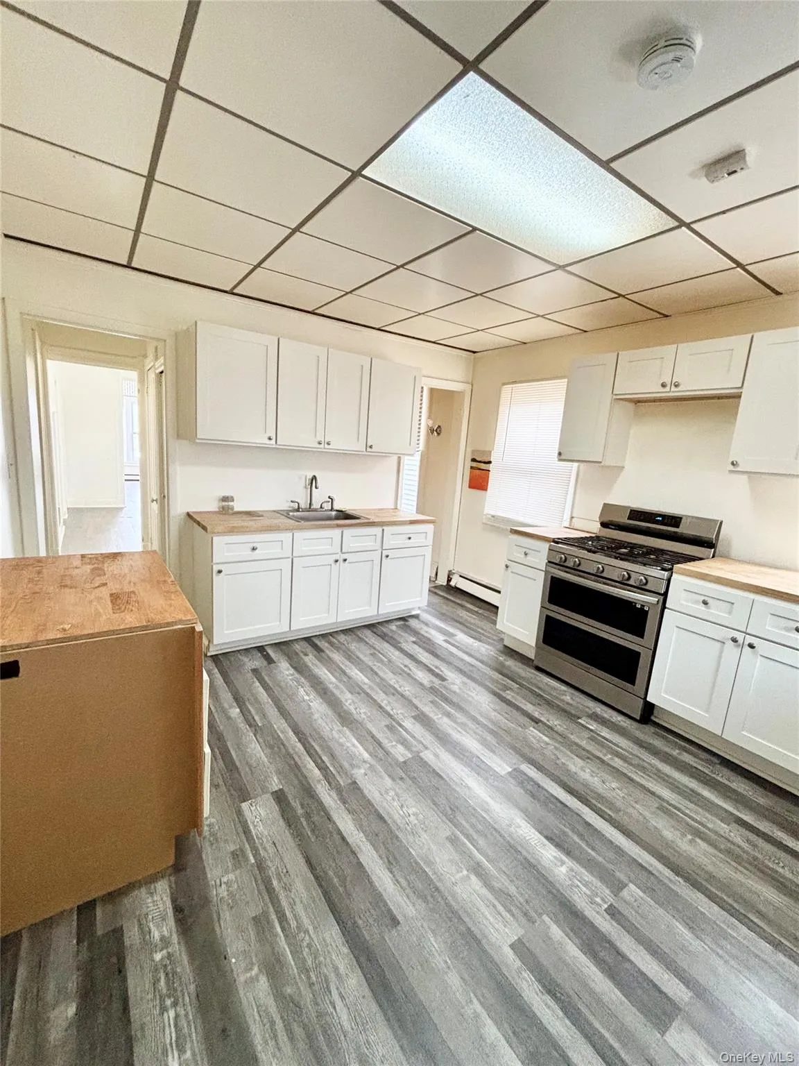 Kitchen featuring white cabinets, double oven range, a paneled ceiling, light wood finished floors, and butcher block countertops Kitchen featuring white cabinets, double oven range, a paneled ceiling, light wood finished floors, and butcher block countertops