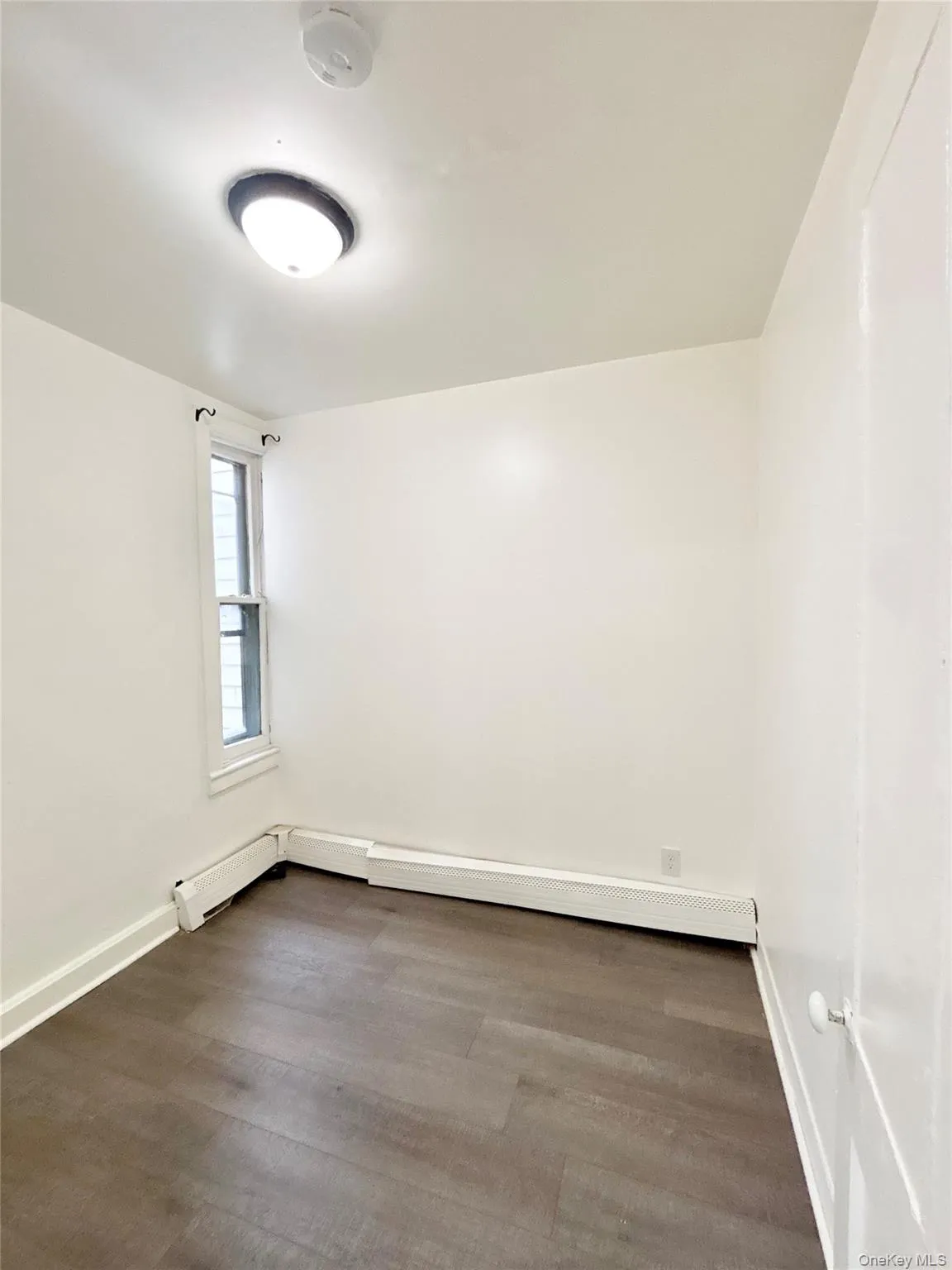 Empty room with dark wood-style floors, a baseboard radiator, and baseboard heating Empty room with dark wood-style floors, a baseboard radiator, and baseboard heating