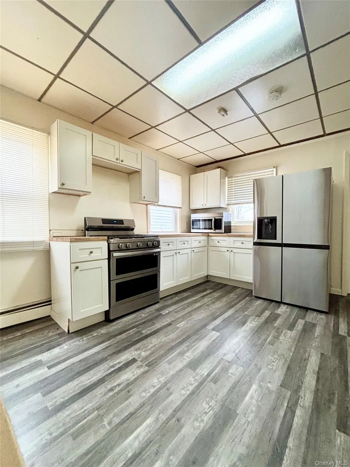 Kitchen with stainless steel appliances, white cabinets, a paneled ceiling, a baseboard heating unit, and light countertops Kitchen with stainless steel appliances, white cabinets, a paneled ceiling, a baseboard heating unit, and light countertops