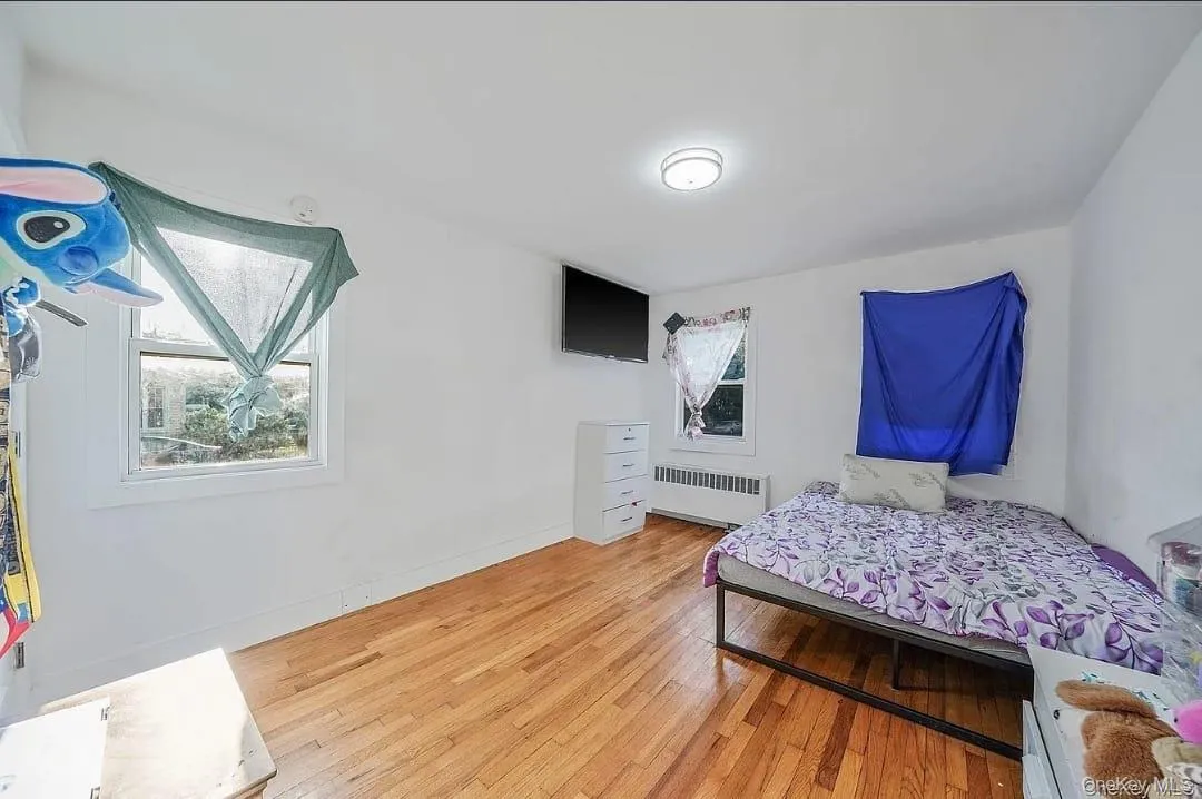Bedroom featuring multiple windows, light wood-type flooring, and radiator Bedroom featuring multiple windows, light wood-type flooring, and radiator