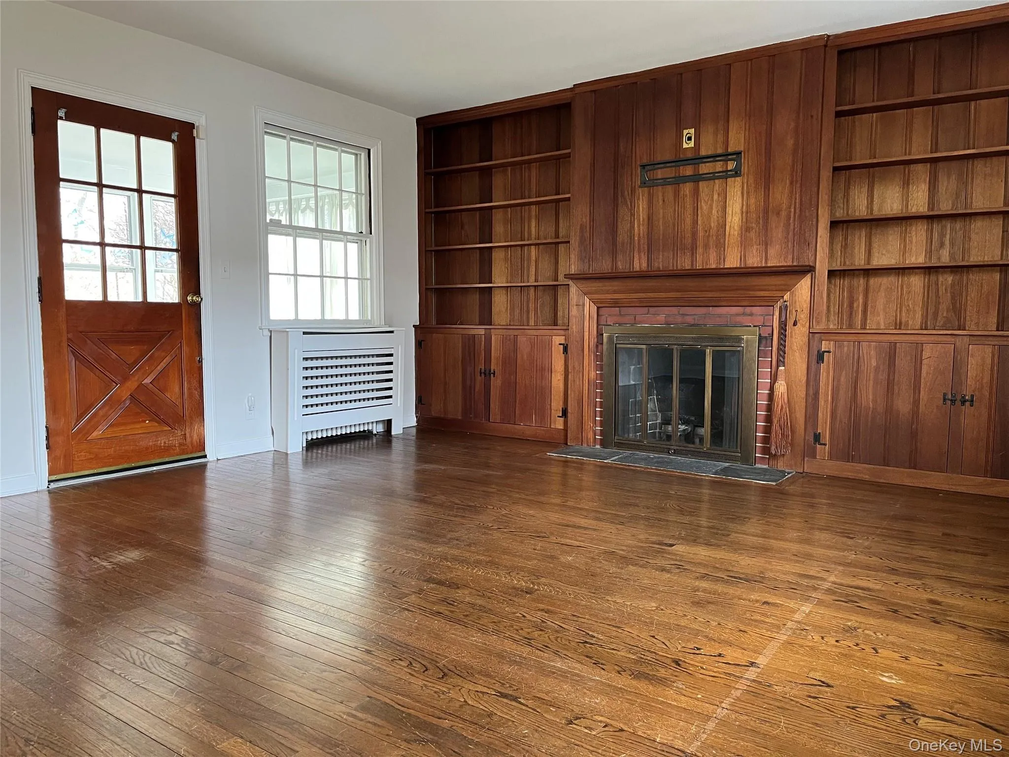 Unfurnished living room with built in features, a fireplace, dark wood finished floors, and radiator Unfurnished living room with built in features, a fireplace, dark wood finished floors, and radiator