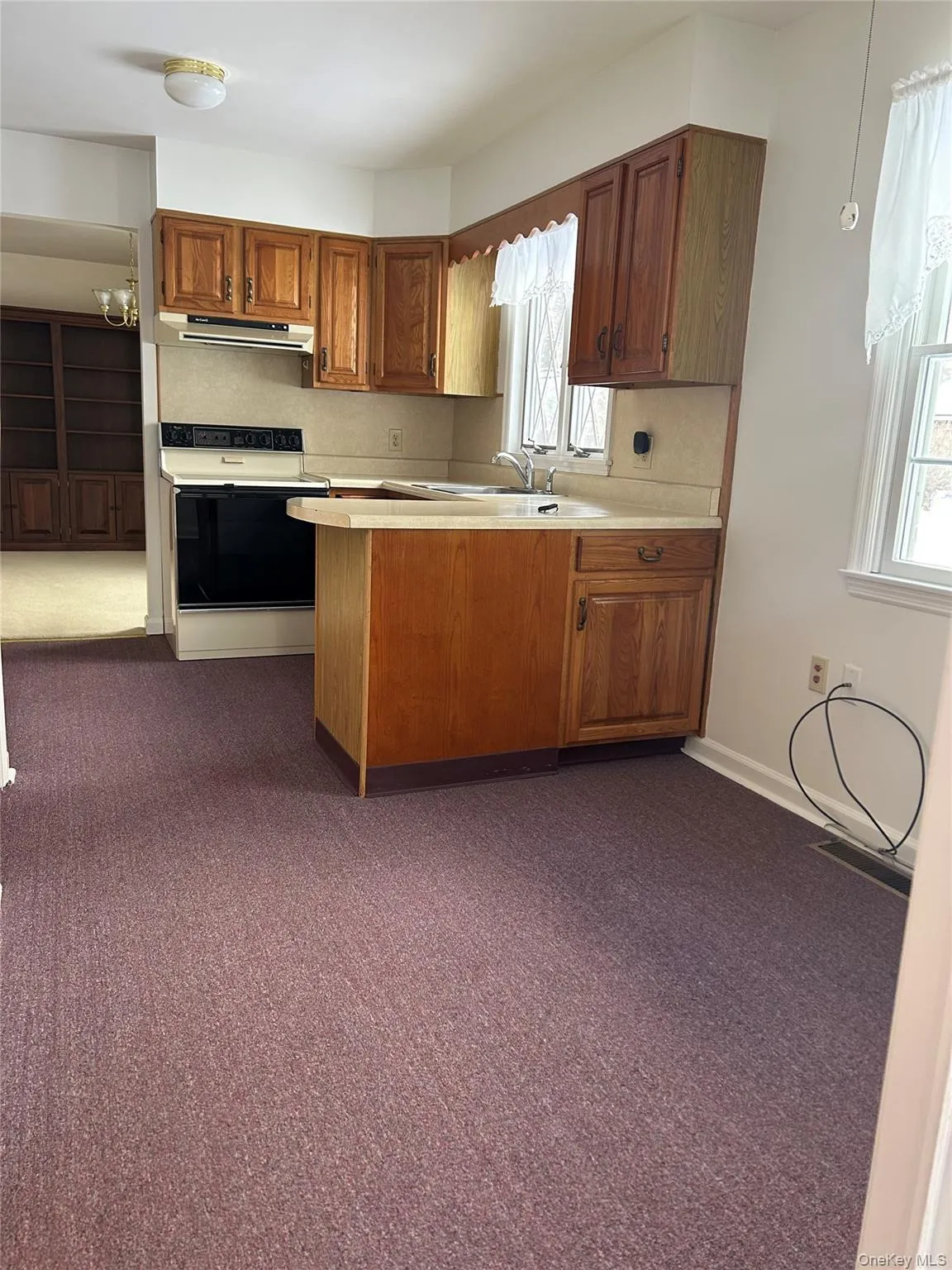 Kitchen with light countertops, dark colored carpet, a peninsula, electric range, and under cabinet range hood Kitchen with light countertops, dark colored carpet, a peninsula, electric range, and under cabinet range hood