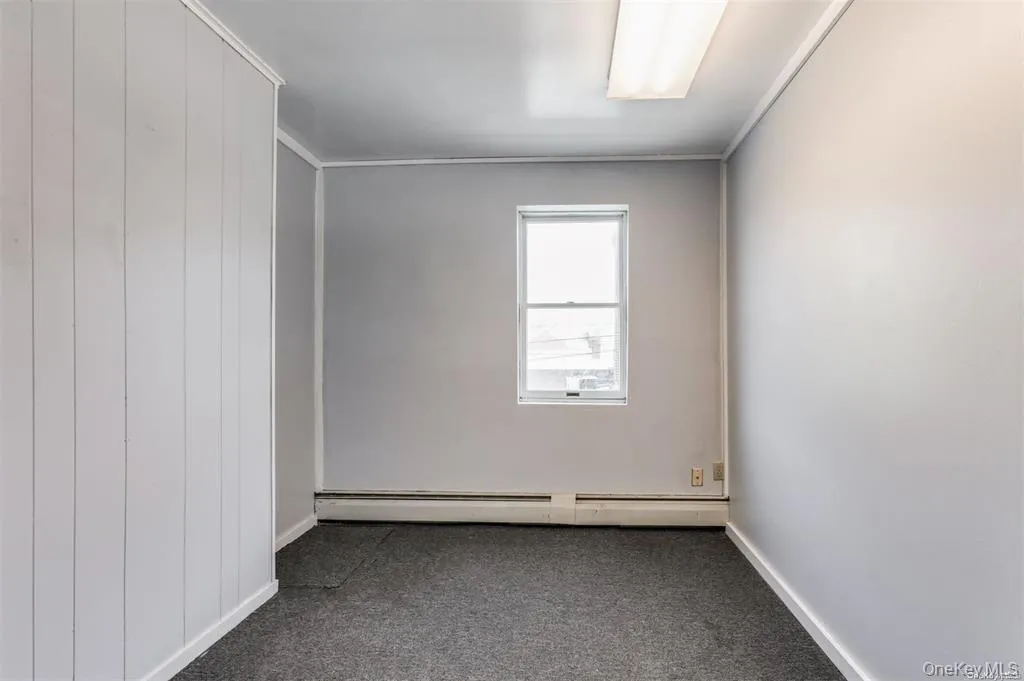 Unfurnished room with dark carpet, a baseboard heating unit, and wood walls Unfurnished room with dark carpet, a baseboard heating unit, and wood walls