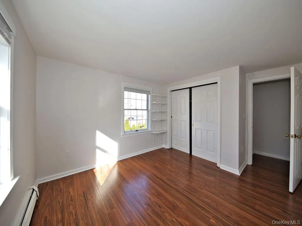 Unfurnished bedroom featuring a baseboard radiator, a closet, and dark wood-style floors Unfurnished bedroom featuring a baseboard radiator, a closet, and dark wood-style floors