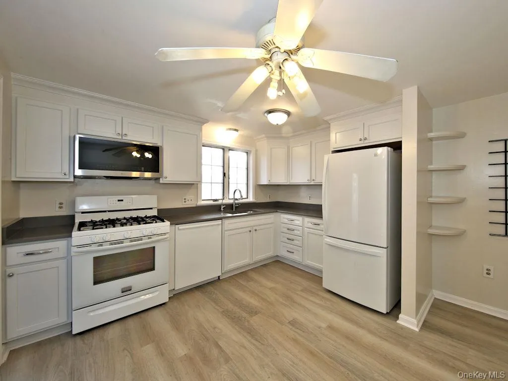 Kitchen with white appliances, dark countertops, ceiling fan, white cabinetry, and light wood-type flooring Kitchen with white appliances, dark countertops, ceiling fan, white cabinetry, and light wood-type flooring