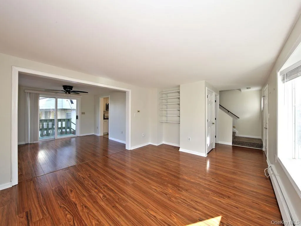 Unfurnished living room featuring baseboard heating, dark wood-style floors, a ceiling fan, and stairway Unfurnished living room featuring baseboard heating, dark wood-style floors, a ceiling fan, and stairway