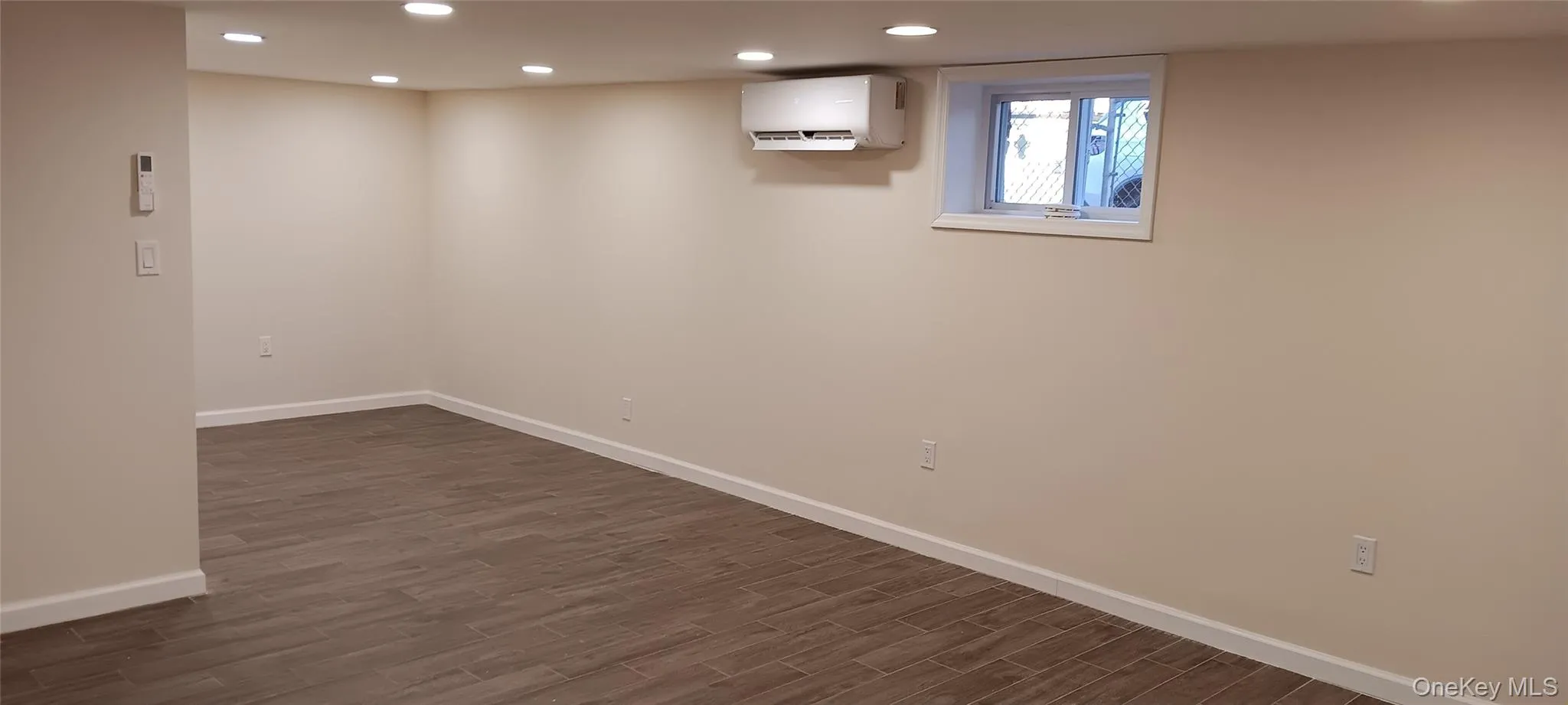 Below grade area featuring recessed lighting, dark wood-style flooring, and a wall mounted AC Below grade area featuring recessed lighting, dark wood-style flooring, and a wall mounted AC