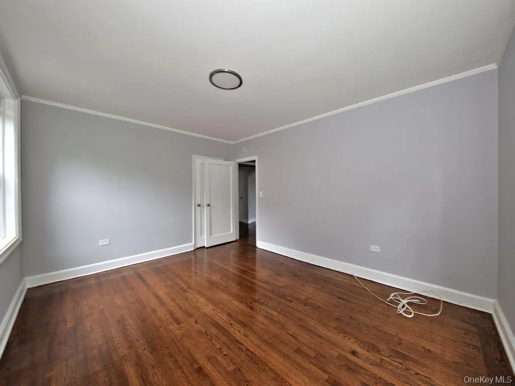 Unfurnished room featuring crown molding and dark wood finished floors Unfurnished room featuring crown molding and dark wood finished floors