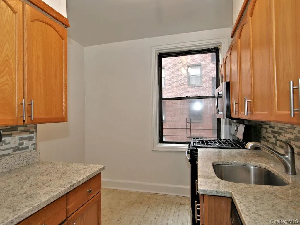 Kitchen featuring decorative backsplash, black range with gas stovetop, light stone counters, and brown cabinets Kitchen featuring decorative backsplash, black range with gas stovetop, light stone counters, and brown cabinets