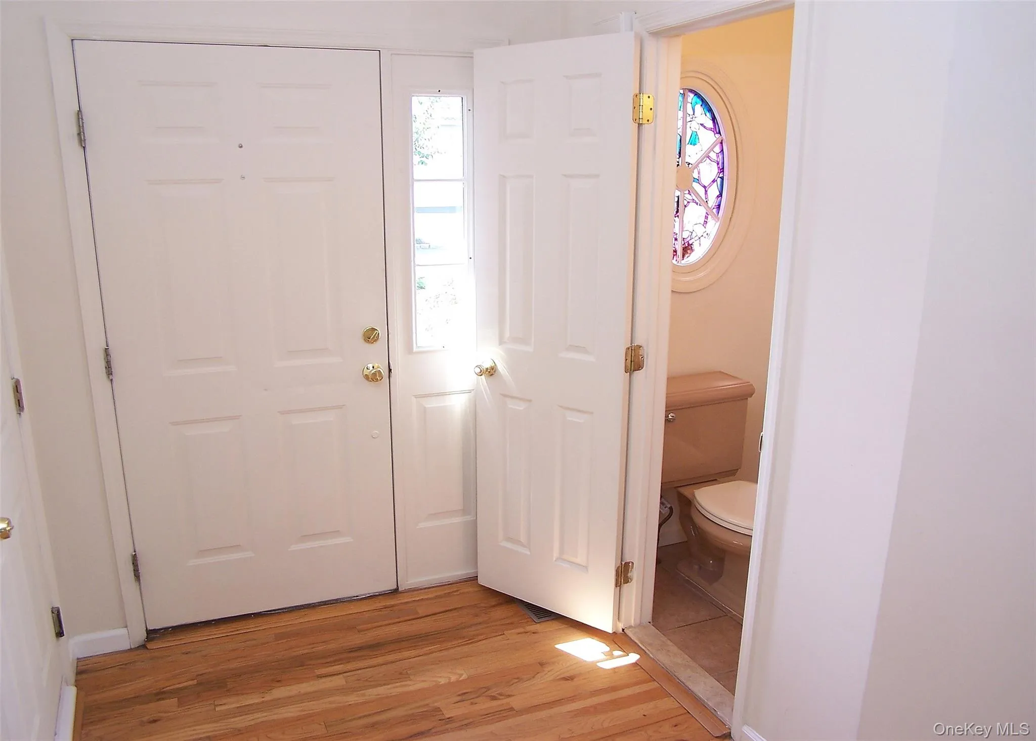 Entrance Foyer With Oak Wood Flooring, Coat Closet, & Access To Half Bath With Deco Stained Glass Oval Window Entrance Foyer With Oak Wood Flooring, Coat Closet, & Access To Half Bath With Deco Stained Glass Oval Window
