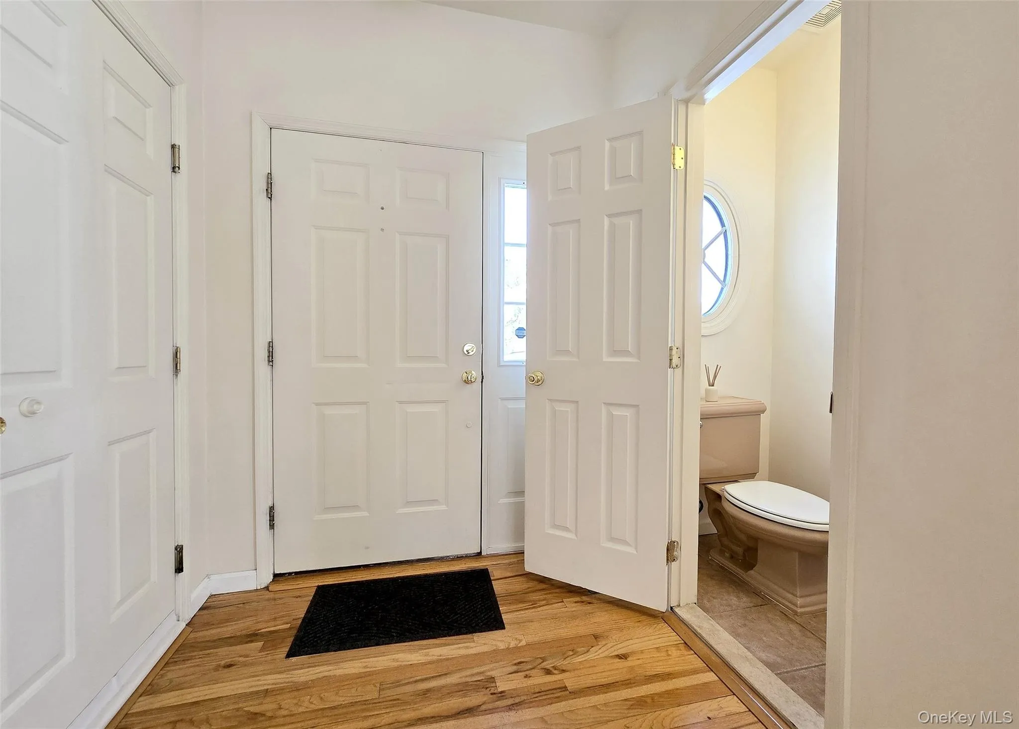 Entrance Foyer With Oak Wood Flooring, Coat Closet, & Access To Half Bath With Deco Stained Glass Oval Window Entrance Foyer With Oak Wood Flooring, Coat Closet, & Access To Half Bath With Deco Stained Glass Oval Window