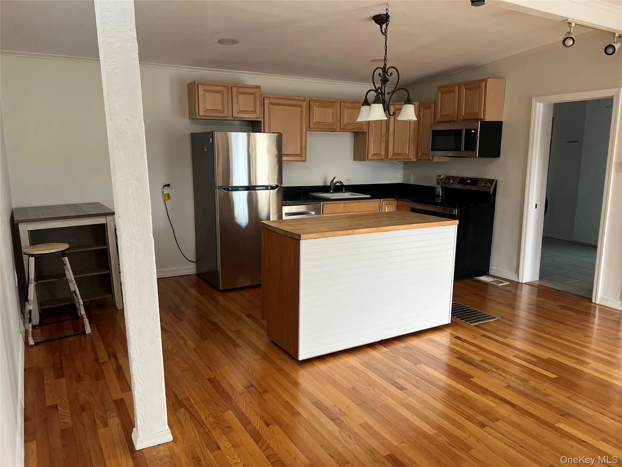 Kitchen with appliances with stainless steel finishes, light wood finished floors, pendant lighting, a kitchen island, and crown molding Kitchen with appliances with stainless steel finishes, light wood finished floors, pendant lighting, a kitchen island, and crown molding
