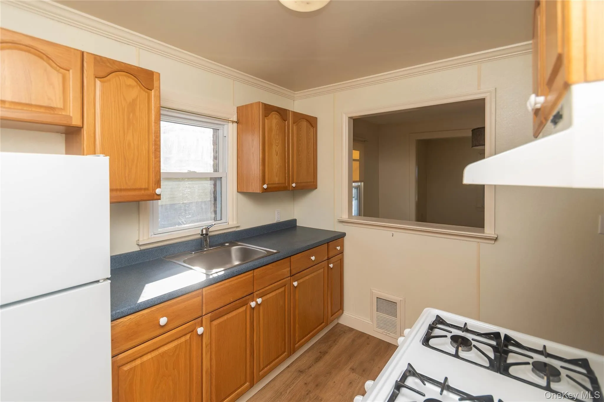 Kitchen featuring white appliances, dark countertops, brown cabinets, ventilation hood, and light wood-style floors Kitchen featuring white appliances, dark countertops, brown cabinets, ventilation hood, and light wood-style floors