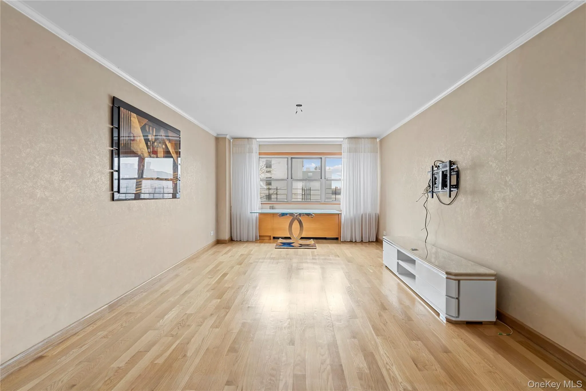 Unfurnished living room featuring a textured wall, light wood-style floors, and ornamental molding Unfurnished living room featuring a textured wall, light wood-style floors, and ornamental molding
