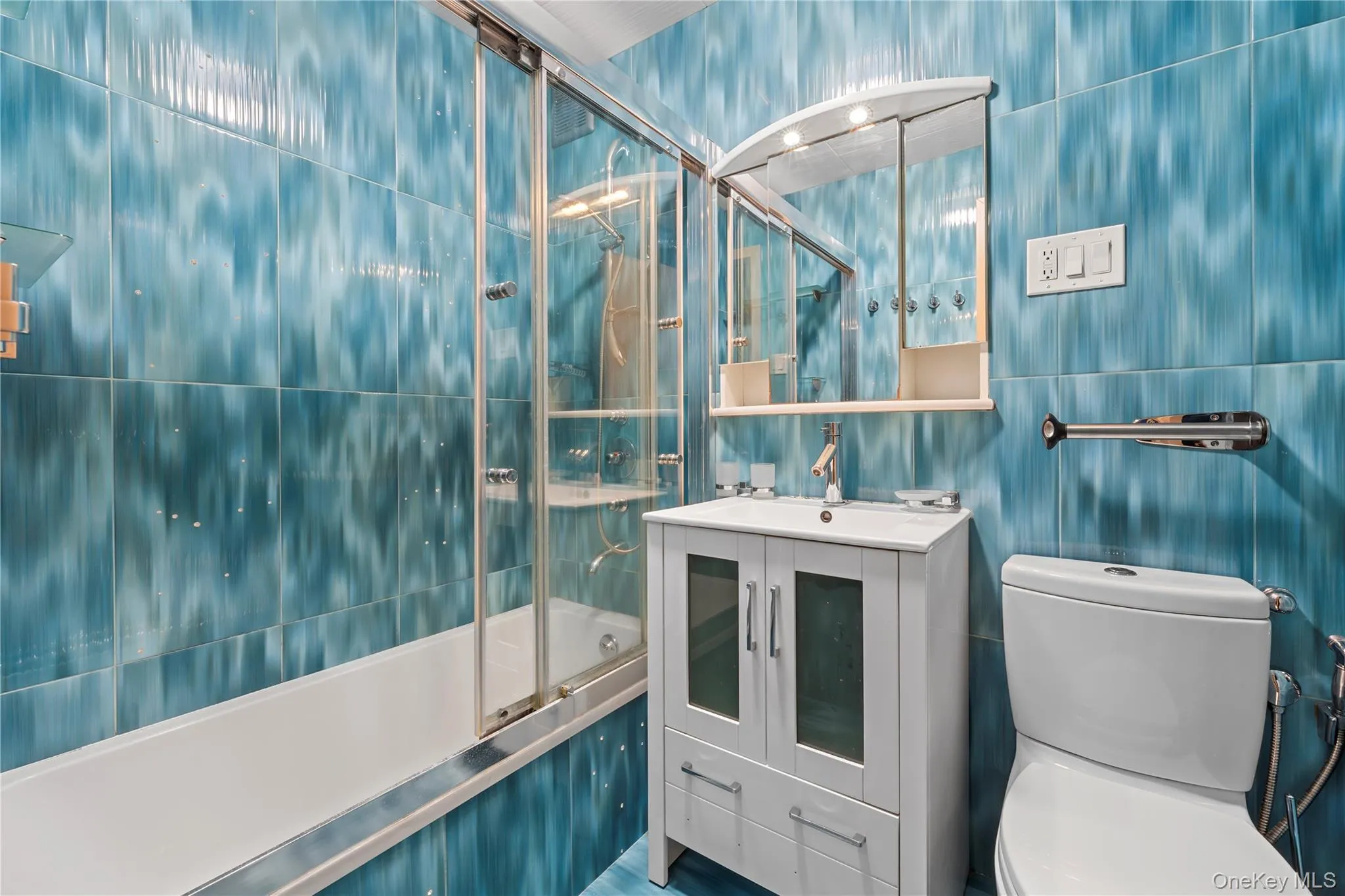 Bathroom with tile walls, bath / shower combo with glass door, and vanity Bathroom with tile walls, bath / shower combo with glass door, and vanity