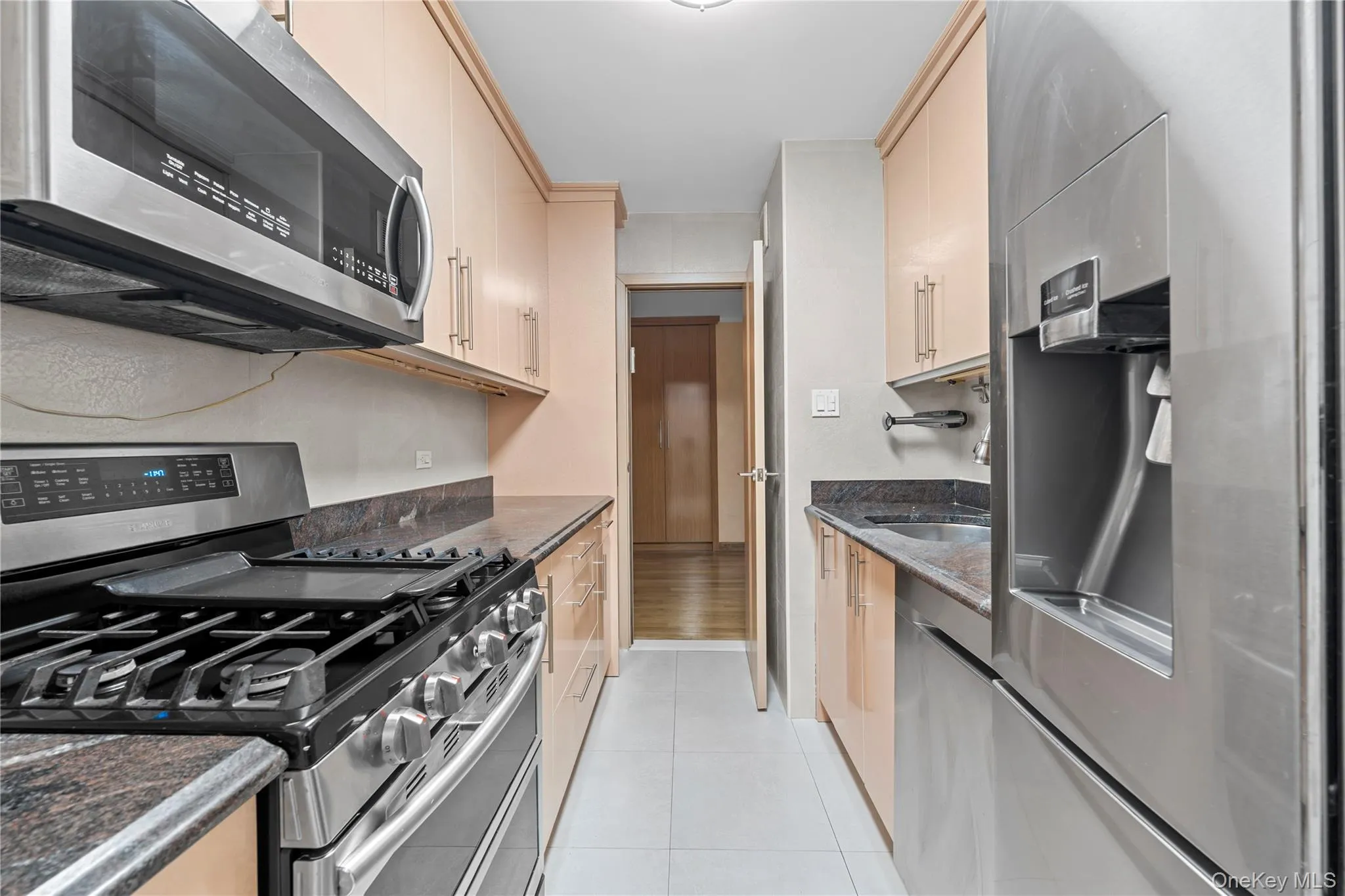 Kitchen with stainless steel appliances, dark stone countertops, light tile patterned flooring, and light brown cabinetry Kitchen with stainless steel appliances, dark stone countertops, light tile patterned flooring, and light brown cabinetry