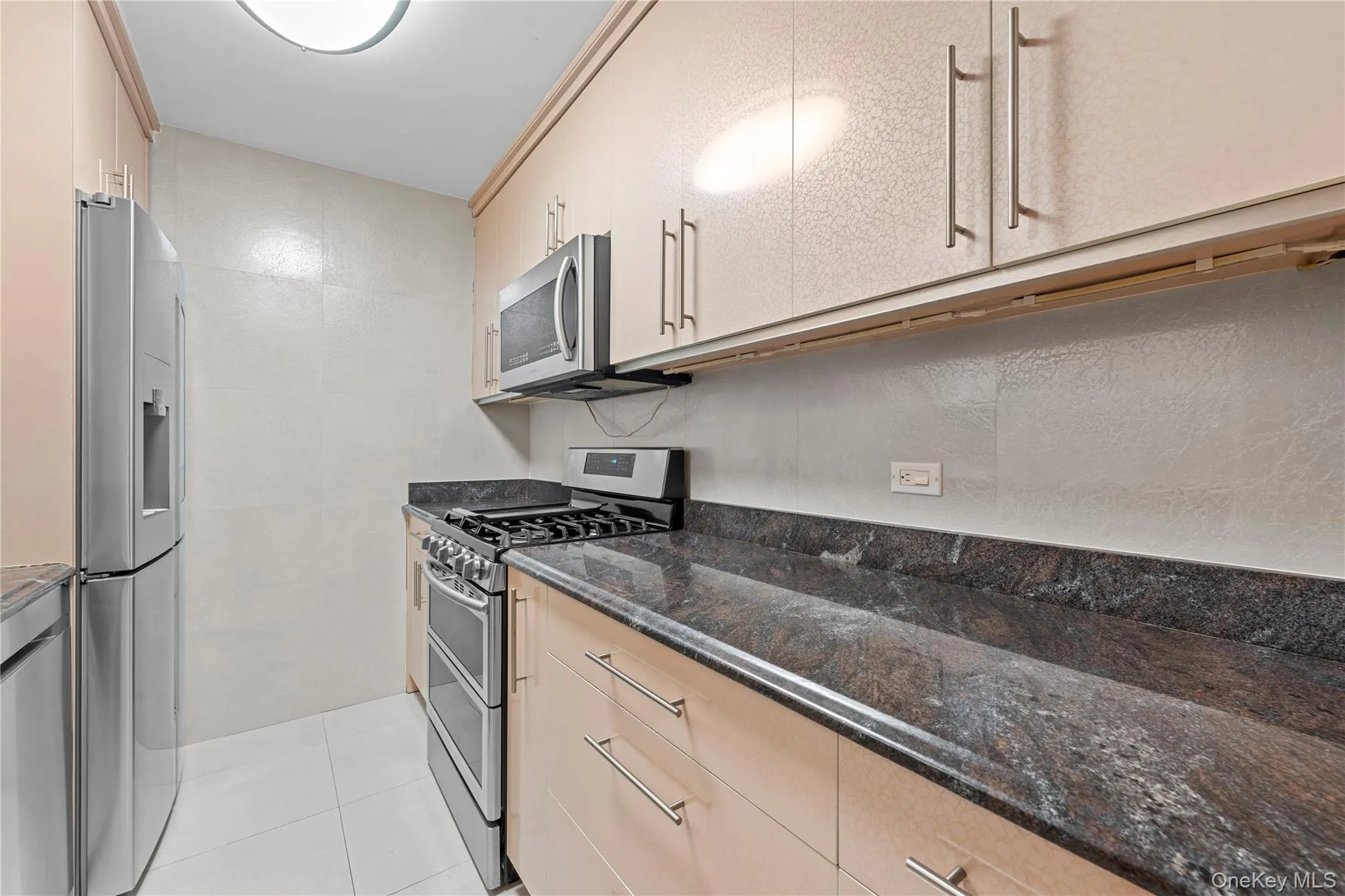 Kitchen featuring appliances with stainless steel finishes, dark stone counters, light tile patterned flooring, and light brown cabinets Kitchen featuring appliances with stainless steel finishes, dark stone counters, light tile patterned flooring, and light brown cabinets