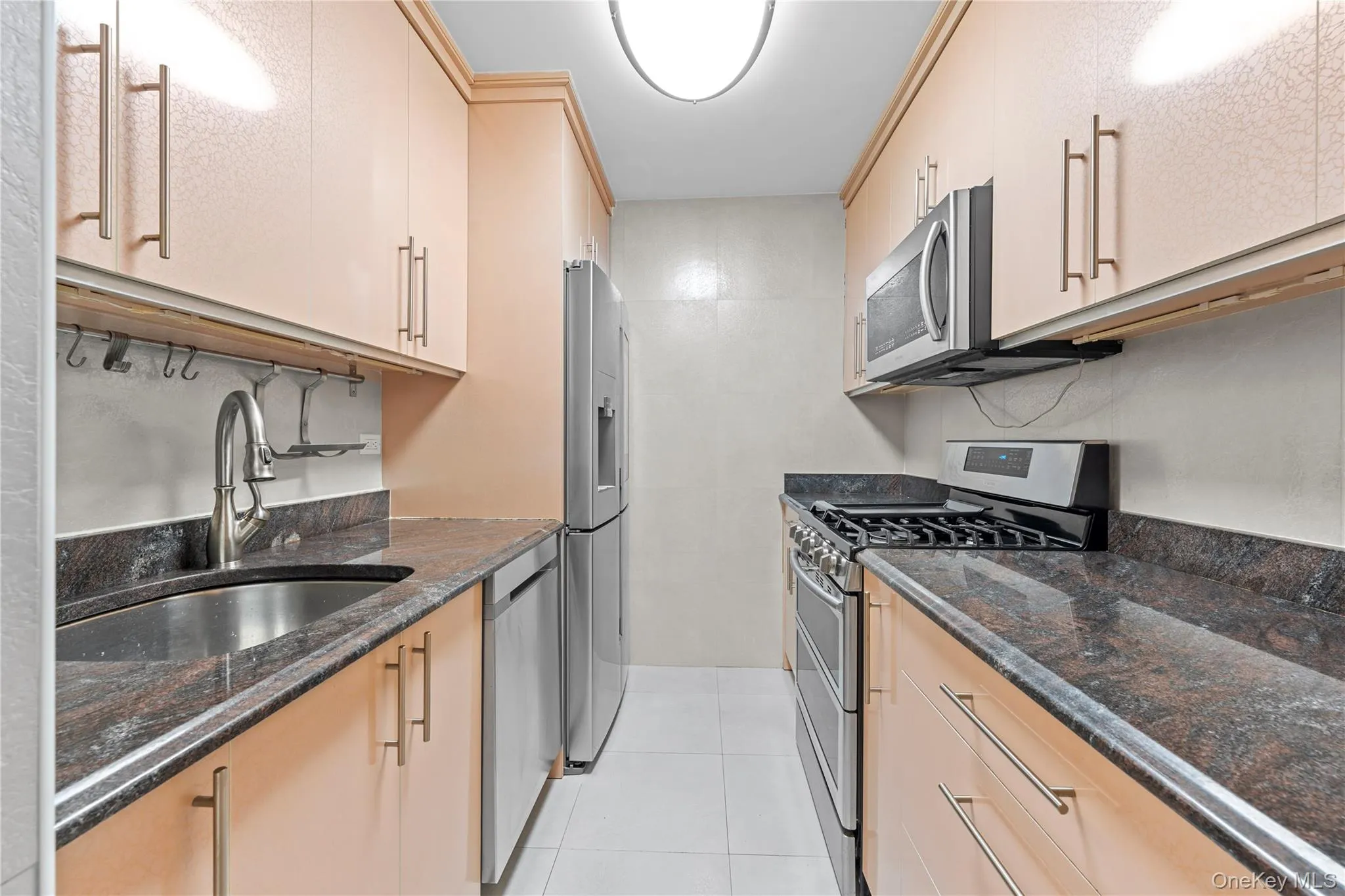 Kitchen featuring appliances with stainless steel finishes, dark stone countertops, light tile patterned floors, and light brown cabinets Kitchen featuring appliances with stainless steel finishes, dark stone countertops, light tile patterned floors, and light brown cabinets