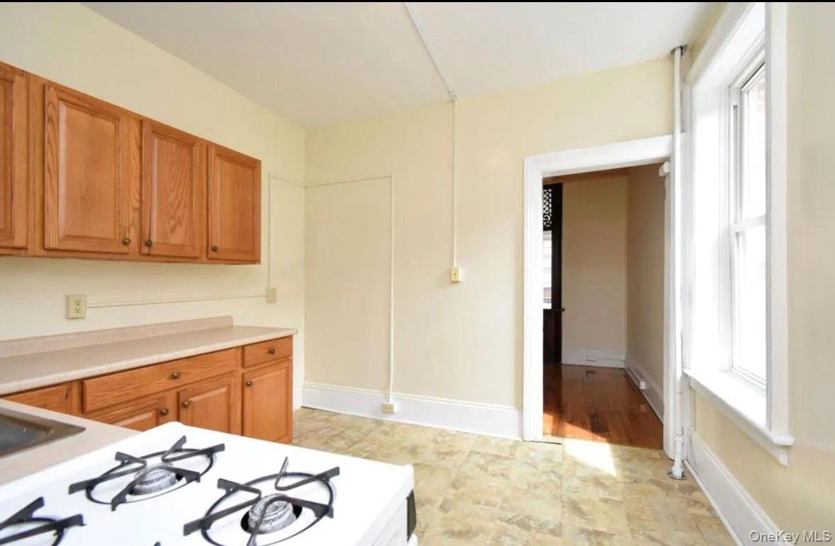 Kitchen with light countertops, white gas stovetop, brown cabinetry, and stone finish flooring Kitchen with light countertops, white gas stovetop, brown cabinetry, and stone finish flooring