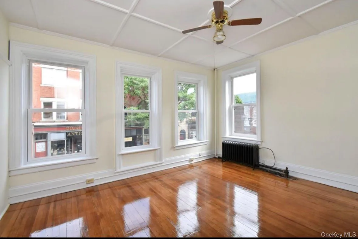 Spare room with a ceiling fan, radiator, and wood-type flooring Spare room with a ceiling fan, radiator, and wood-type flooring