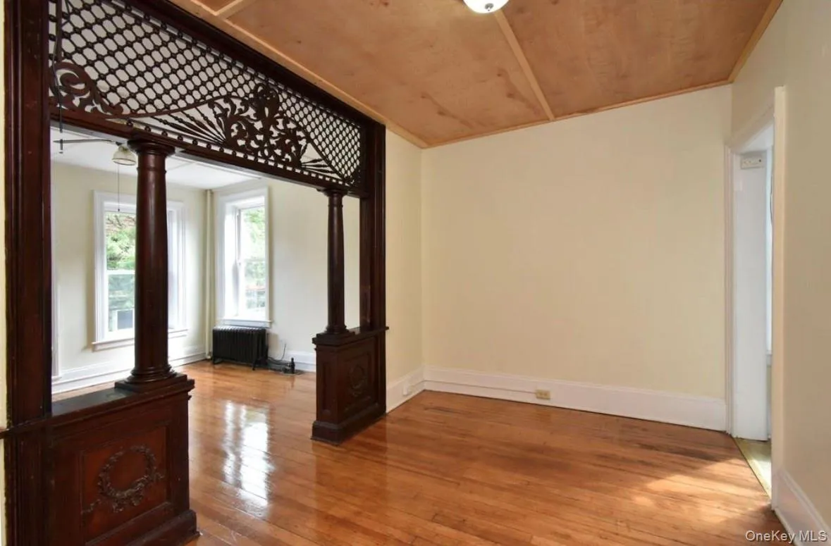 Unfurnished room featuring wood-type flooring, radiator heating unit, wooden ceiling, and decorative columns Unfurnished room featuring wood-type flooring, radiator heating unit, wooden ceiling, and decorative columns