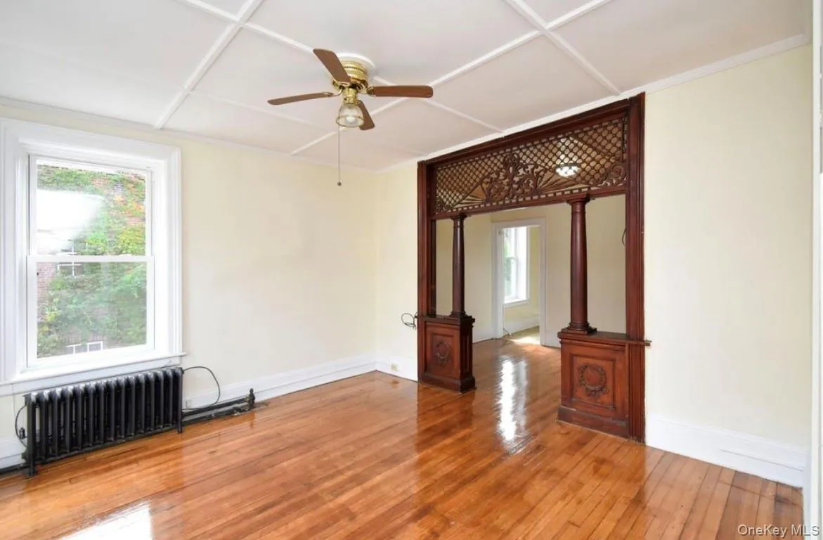 Unfurnished room featuring radiator heating unit, hardwood / wood-style flooring, and a ceiling fan Unfurnished room featuring radiator heating unit, hardwood / wood-style flooring, and a ceiling fan