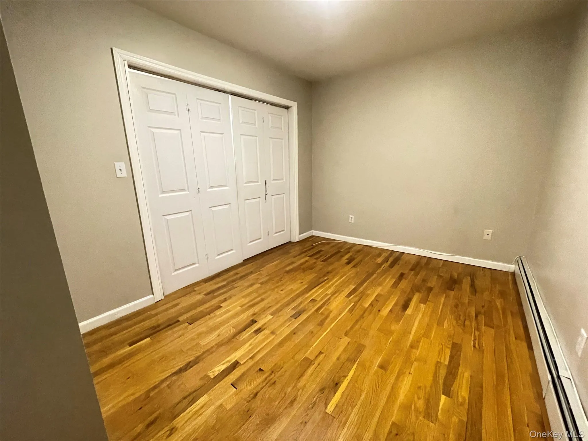 Unfurnished bedroom with a baseboard heating unit, wood finished floors, and a closet Unfurnished bedroom with a baseboard heating unit, wood finished floors, and a closet