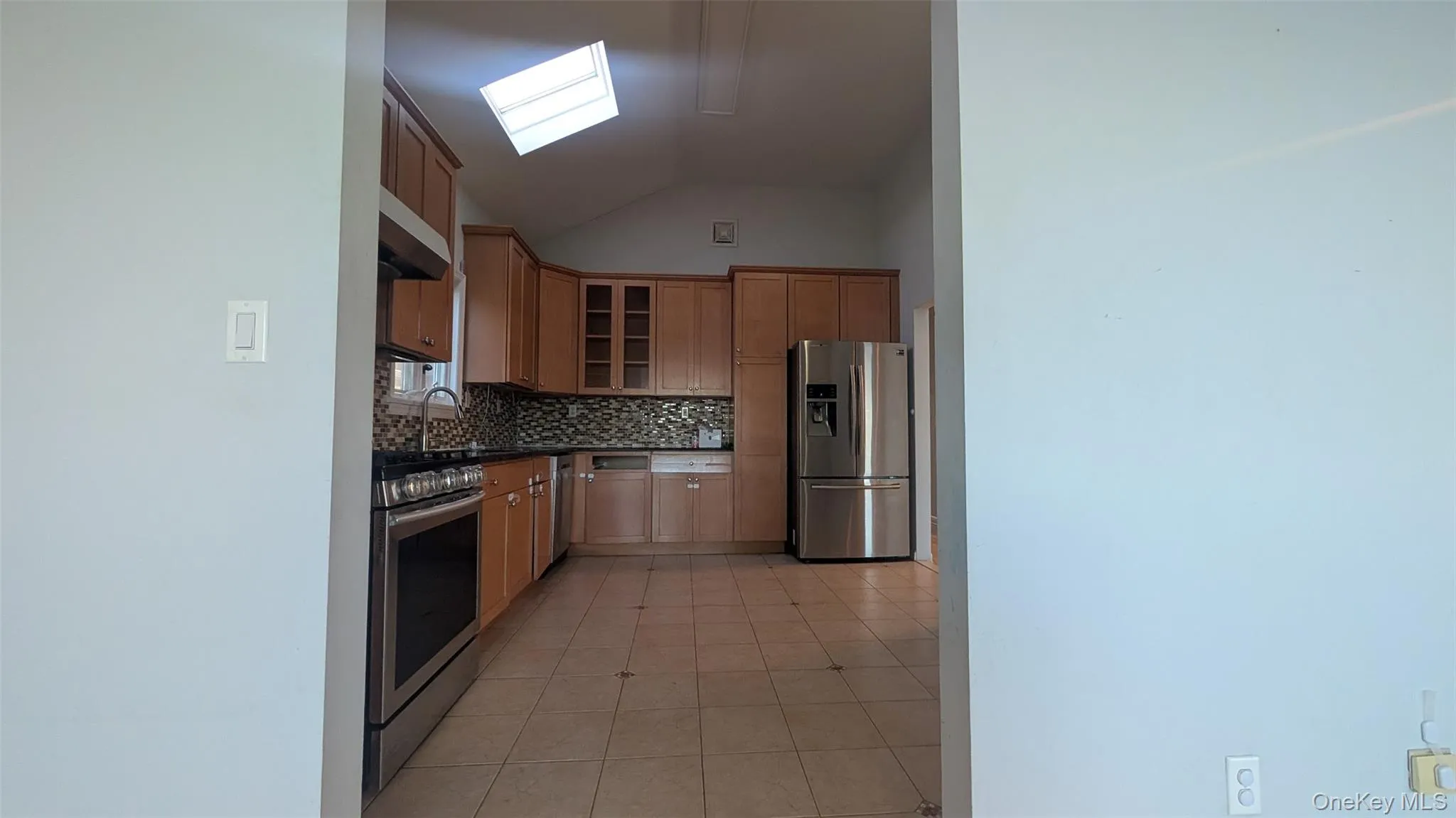 Kitchen with lofted ceiling, appliances with stainless steel finishes, dark countertops, glass insert cabinets, and light tile patterned floors Kitchen with lofted ceiling, appliances with stainless steel finishes, dark countertops, glass insert cabinets, and light tile patterned floors