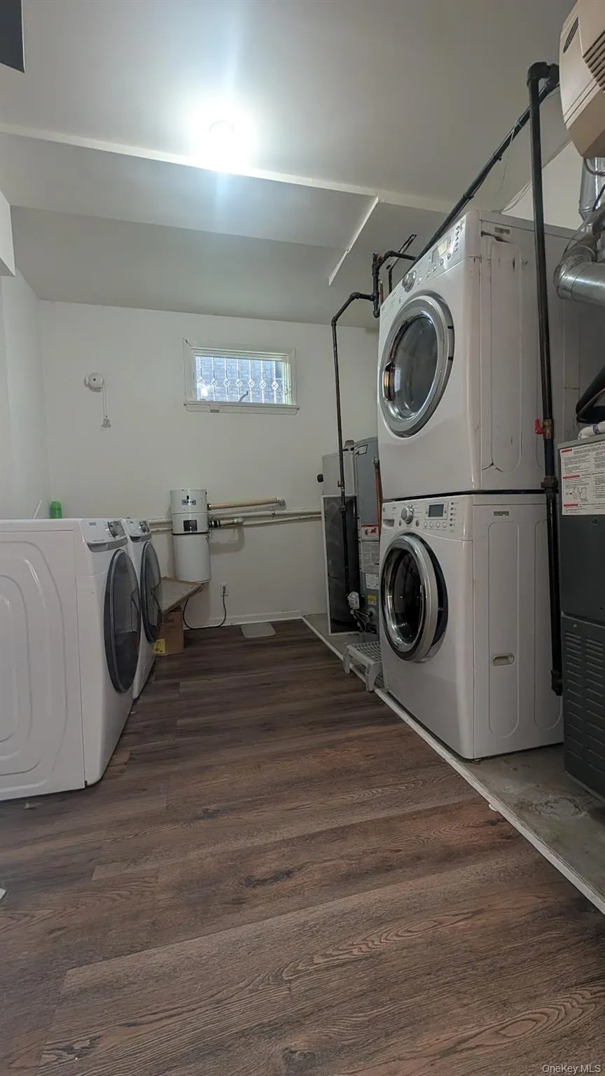 Laundry room featuring dark wood-style floors, stacked washer and clothes dryer, and gas water heater Laundry room featuring dark wood-style floors, stacked washer and clothes dryer, and gas water heater