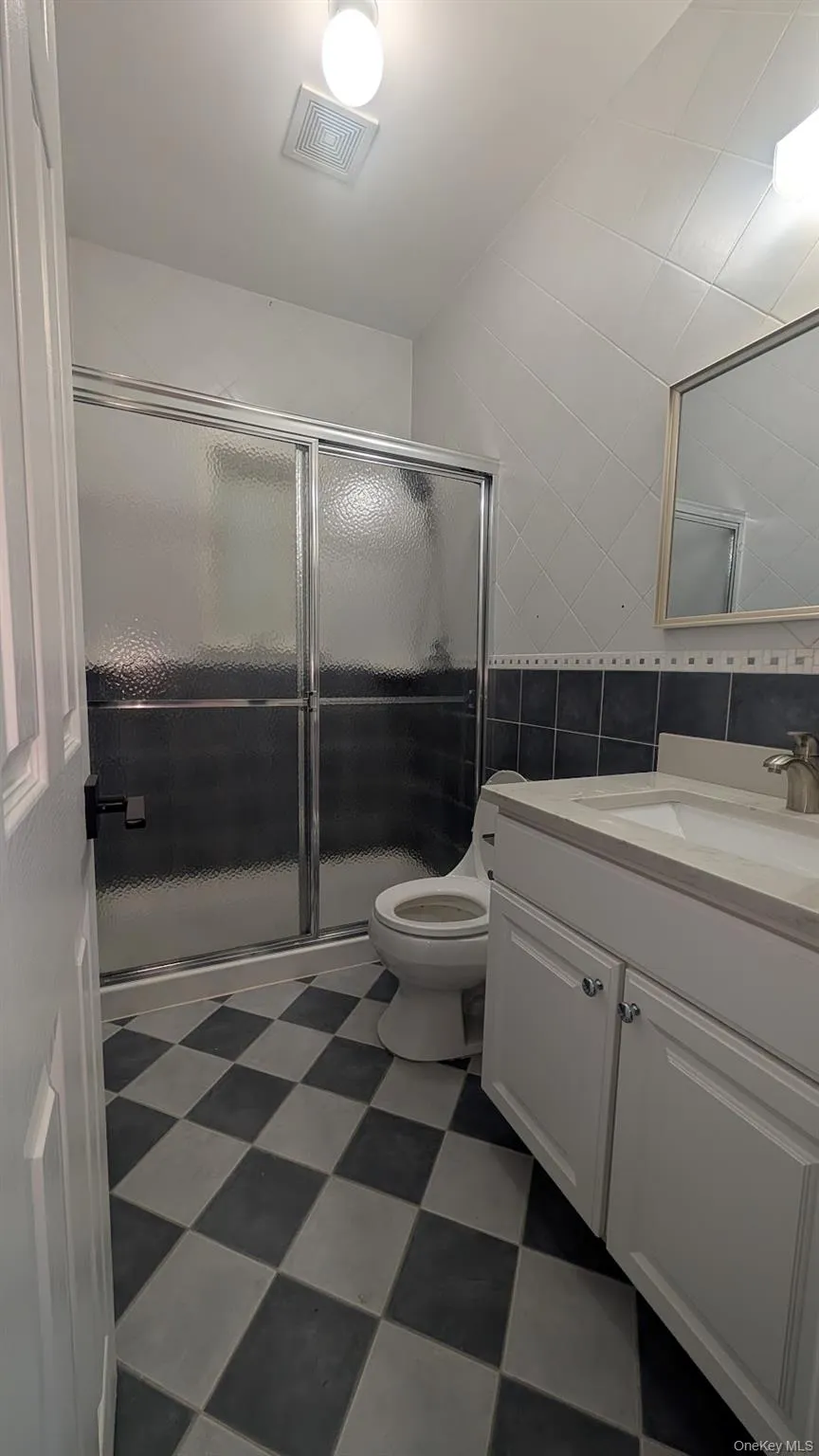 Bathroom featuring dark floors, tile walls, vanity, and a stall shower Bathroom featuring dark floors, tile walls, vanity, and a stall shower
