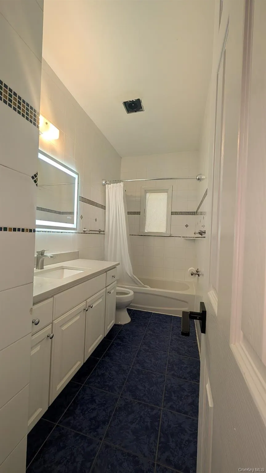 Full bathroom featuring vanity, shower / bath combo with shower curtain, dark tile patterned flooring, and tile walls Full bathroom featuring vanity, shower / bath combo with shower curtain, dark tile patterned flooring, and tile walls